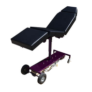 A purple tattoo chair with black vinyl upholstery, manual adjustable top frame, and solid rubber wheels.